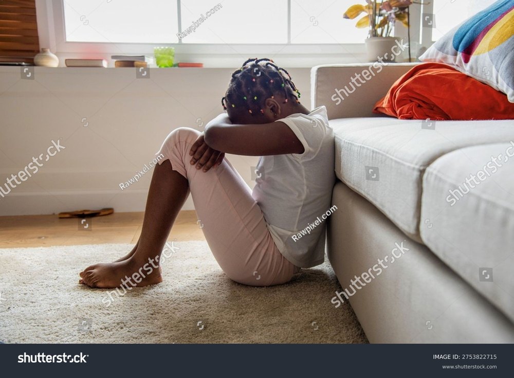 A young girl curled on the floor against a couch